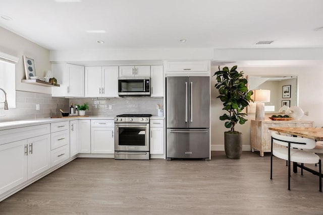 kitchen with white cabinetry, appliances with stainless steel finishes, backsplash, light hardwood / wood-style flooring, and sink