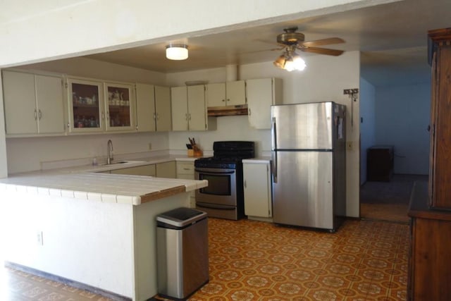 kitchen featuring stainless steel appliances, sink, ceiling fan, kitchen peninsula, and tile counters