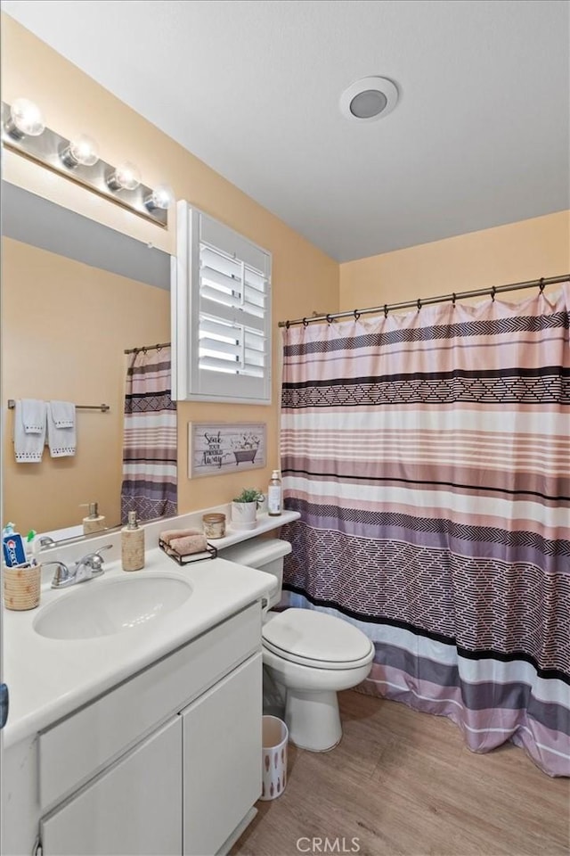 full bath with a shower with curtain, vanity, toilet, and wood finished floors