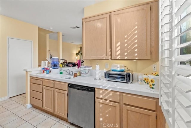 kitchen with light tile patterned floors, stainless steel dishwasher, and light brown cabinets