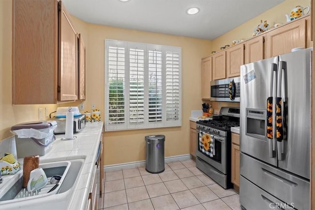 kitchen with tile countertops, light tile patterned floors, stainless steel appliances, light brown cabinetry, and baseboards