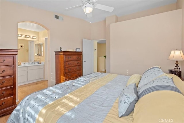 bedroom featuring arched walkways, visible vents, ensuite bathroom, light wood-style floors, and ceiling fan