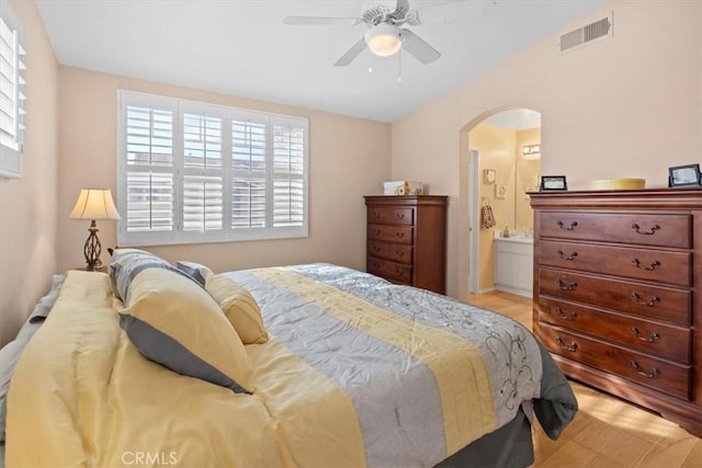 bedroom featuring visible vents, arched walkways, ensuite bath, light wood-style flooring, and ceiling fan