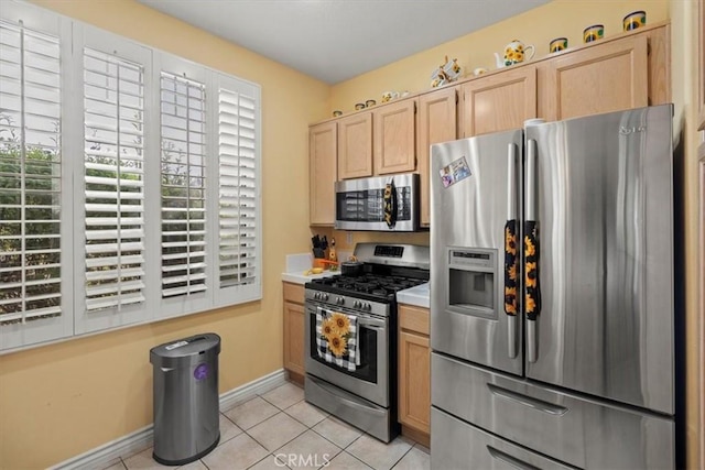 kitchen featuring baseboards, appliances with stainless steel finishes, light countertops, light brown cabinetry, and light tile patterned flooring