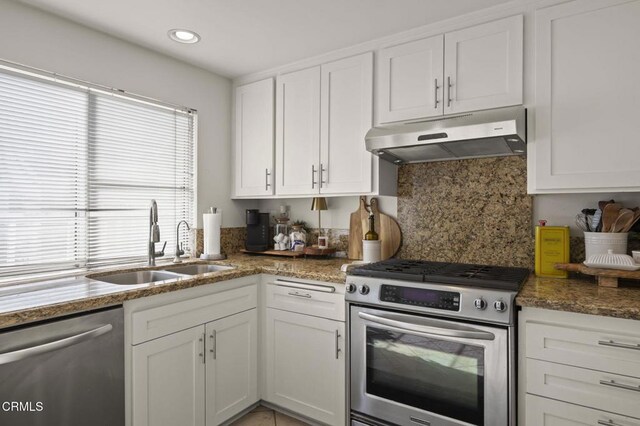 kitchen featuring white cabinetry, stainless steel appliances, dark stone countertops, sink, and backsplash