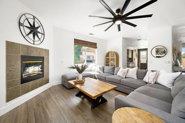 living room featuring ceiling fan, hardwood / wood-style floors, and a tiled fireplace