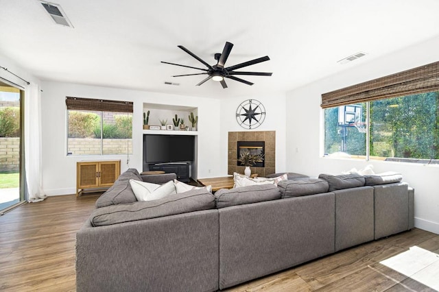 living room featuring ceiling fan, hardwood / wood-style floors, built in features, and a fireplace