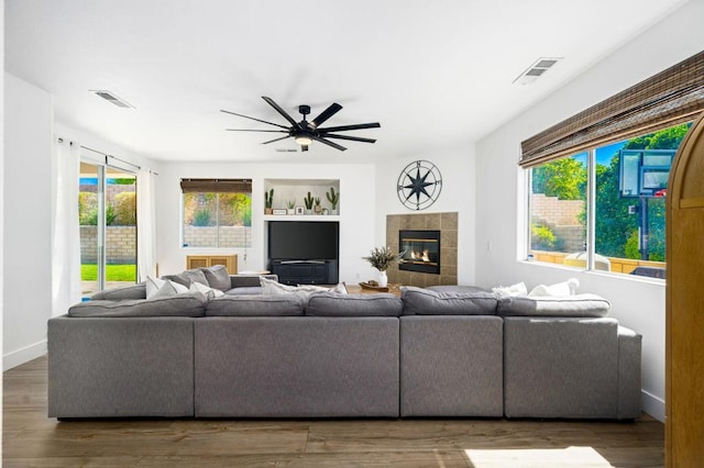 living room with ceiling fan, built in shelves, a fireplace, and dark wood-type flooring