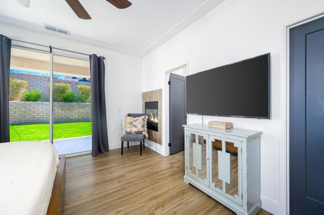 bedroom with access to outside, ceiling fan, a fireplace, and light hardwood / wood-style flooring