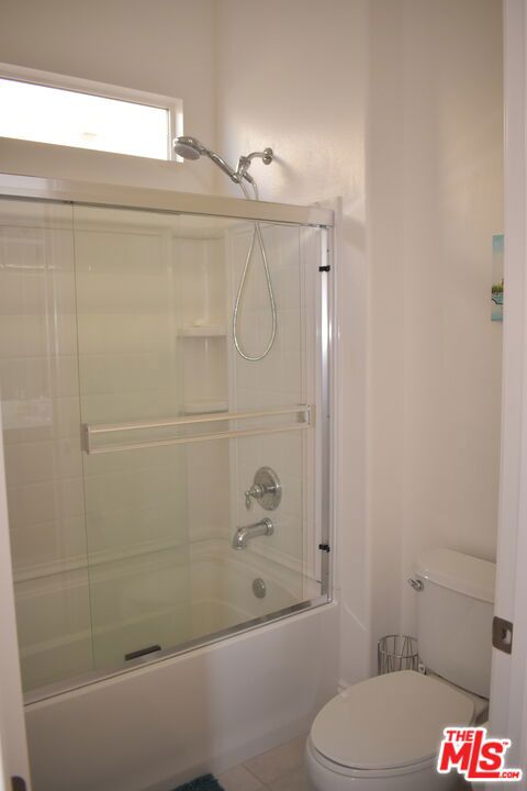 bathroom featuring tile patterned floors, shower / bath combination with glass door, and toilet