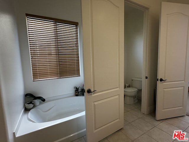 bathroom with a washtub, toilet, and tile patterned flooring