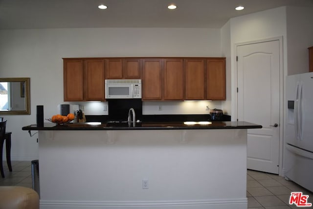 kitchen with white appliances, sink, a kitchen island with sink, a breakfast bar, and light tile patterned floors