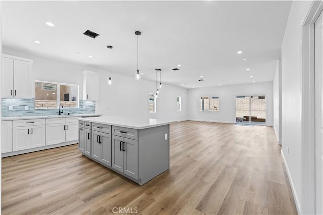 kitchen featuring a kitchen island, decorative light fixtures, white cabinetry, tasteful backsplash, and sink