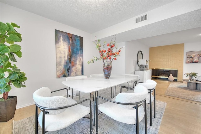 dining area with a large fireplace, a textured ceiling, and light hardwood / wood-style floors