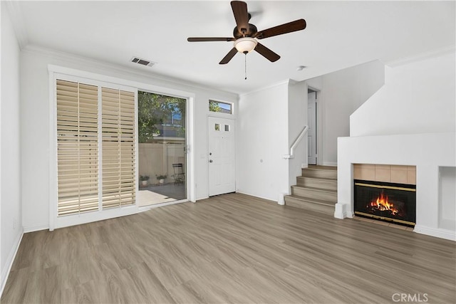 unfurnished living room featuring ceiling fan, hardwood / wood-style floors, ornamental molding, and a tiled fireplace