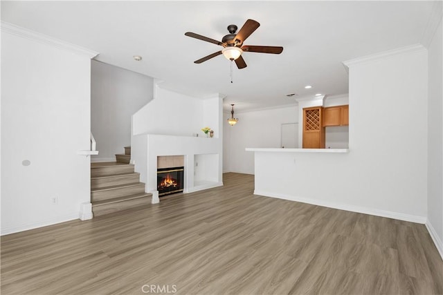 unfurnished living room with hardwood / wood-style flooring, a tile fireplace, ornamental molding, and ceiling fan