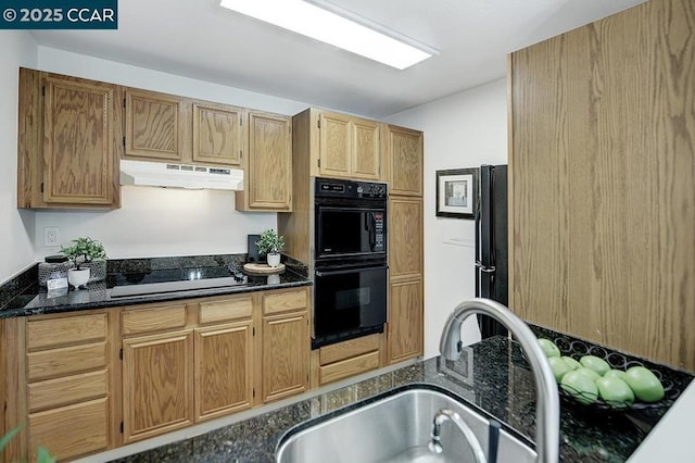 kitchen featuring stovetop, double oven, dark stone countertops, and sink