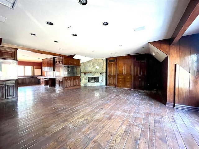 unfurnished living room featuring dark hardwood / wood-style flooring, wood walls, and a stone fireplace