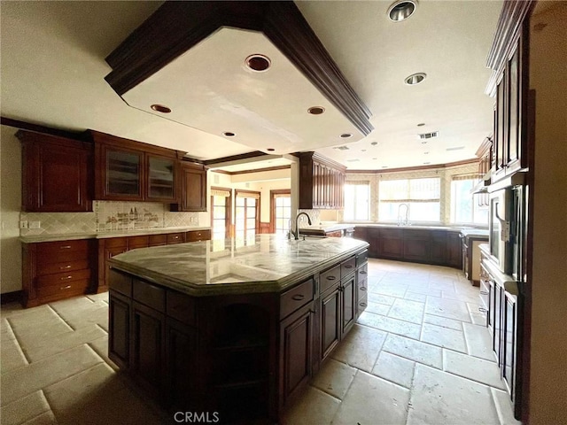 kitchen with sink, backsplash, ornamental molding, a center island with sink, and dark brown cabinets