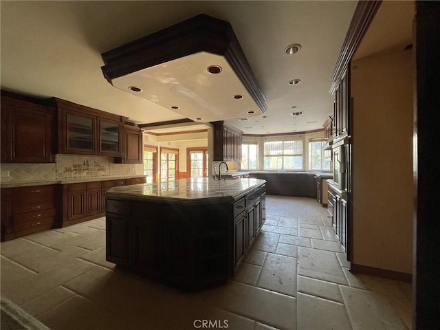 kitchen with sink, dark brown cabinets, an island with sink, and decorative backsplash