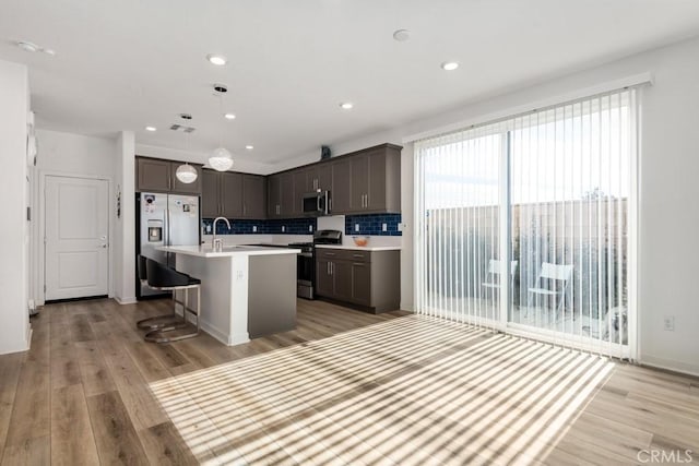 kitchen featuring a breakfast bar, stainless steel appliances, light countertops, backsplash, and light wood-type flooring