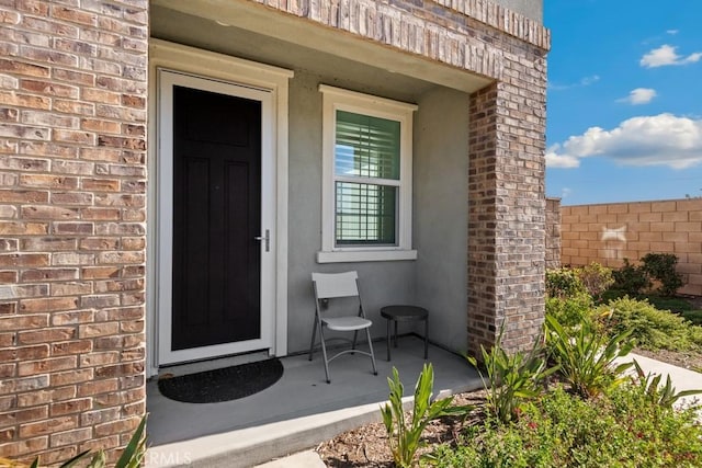 doorway to property featuring brick siding and fence