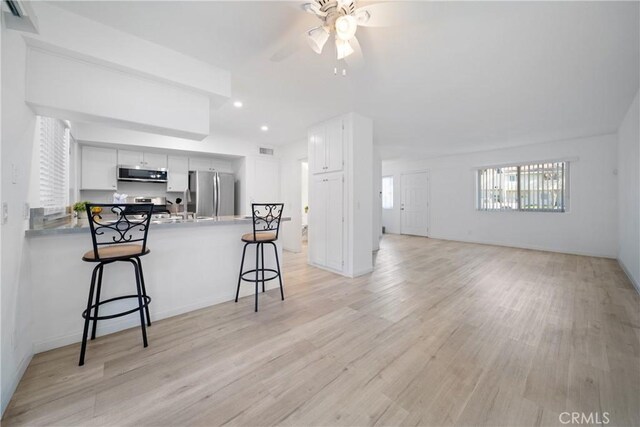 kitchen featuring a kitchen bar, kitchen peninsula, stainless steel appliances, light wood-type flooring, and white cabinets