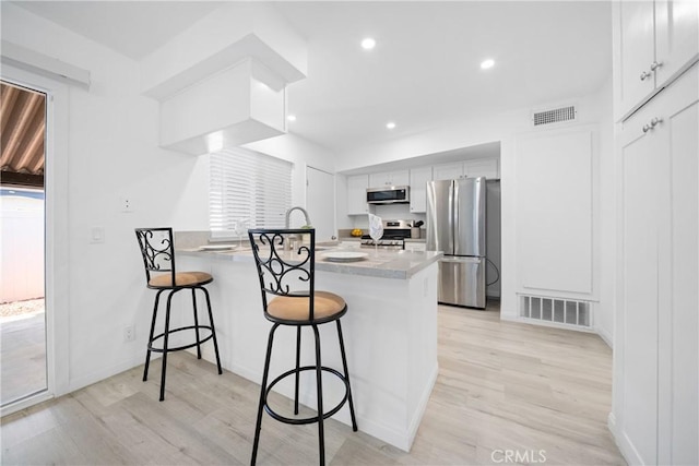 kitchen with light hardwood / wood-style floors, kitchen peninsula, appliances with stainless steel finishes, white cabinets, and a breakfast bar