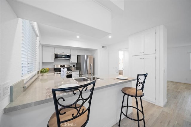 kitchen with kitchen peninsula, sink, white cabinetry, a kitchen breakfast bar, and stainless steel appliances