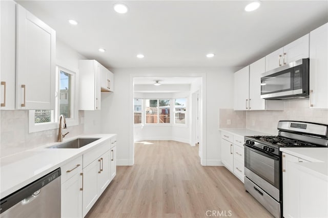 kitchen with appliances with stainless steel finishes, plenty of natural light, light wood-type flooring, white cabinets, and sink