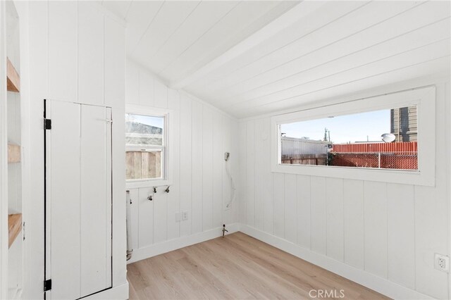 unfurnished room featuring vaulted ceiling, wooden walls, and light hardwood / wood-style flooring