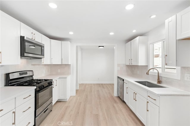 kitchen with white cabinets, appliances with stainless steel finishes, decorative backsplash, sink, and light wood-type flooring