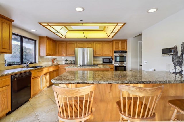 kitchen with light tile patterned floors, sink, appliances with stainless steel finishes, a kitchen breakfast bar, and dark stone counters