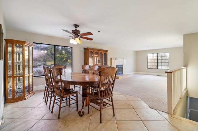 dining room with ceiling fan, light colored carpet, and a tile fireplace