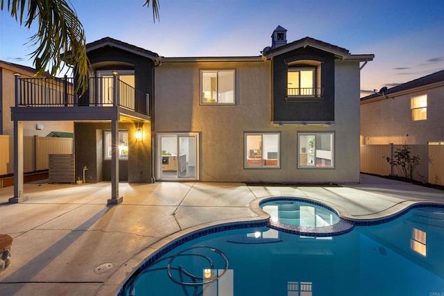 back house at dusk with a balcony, a patio area, and a pool with hot tub