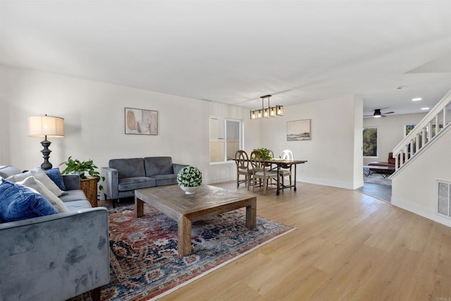 living room featuring ceiling fan with notable chandelier and light wood-type flooring