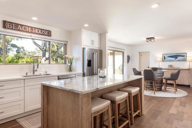 kitchen with sink, white cabinetry, light stone counters, a center island, and appliances with stainless steel finishes