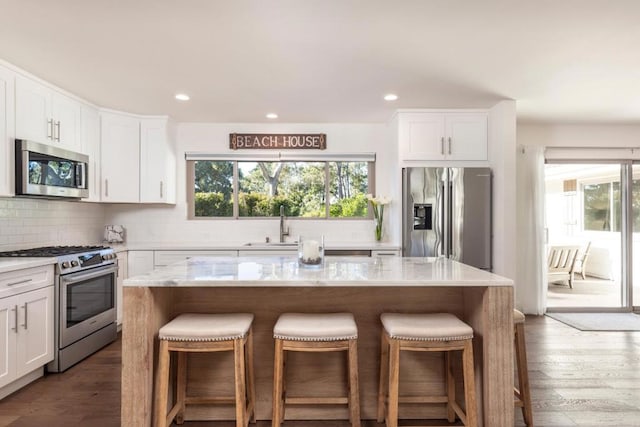 kitchen with white cabinets, decorative backsplash, a center island, stainless steel appliances, and light stone countertops