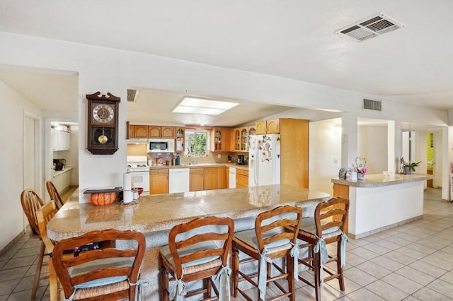 kitchen featuring light tile patterned floors, kitchen peninsula, white appliances, and a breakfast bar area