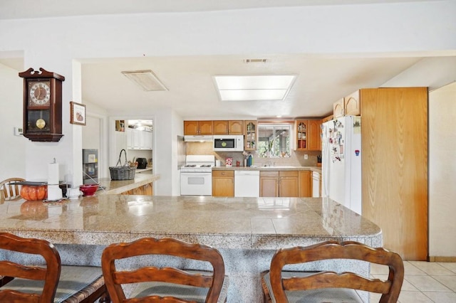 kitchen featuring a kitchen breakfast bar, white appliances, light tile patterned floors, and kitchen peninsula