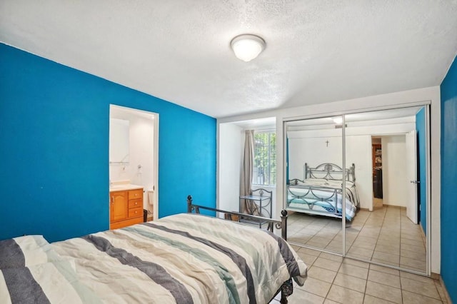 bedroom with ensuite bathroom, light tile patterned floors, and a textured ceiling