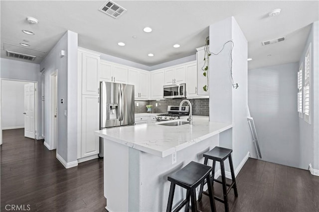 kitchen featuring white cabinetry, kitchen peninsula, stainless steel appliances, a kitchen breakfast bar, and sink