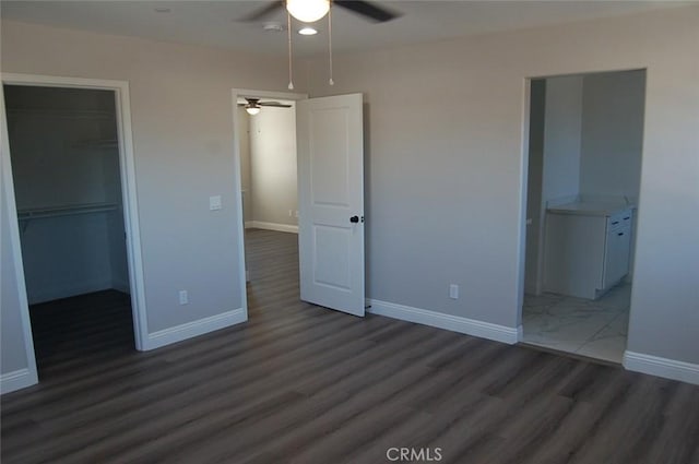 unfurnished bedroom with dark wood-type flooring, a closet, a spacious closet, and ceiling fan