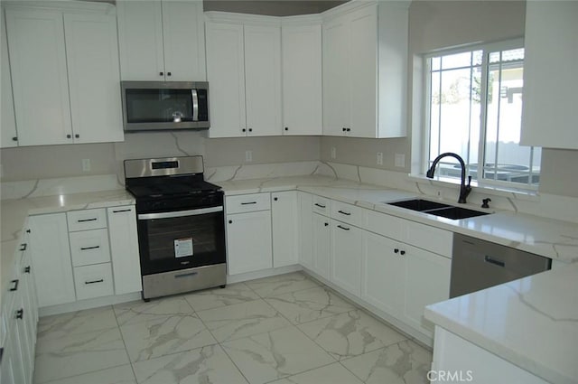 kitchen featuring appliances with stainless steel finishes, white cabinets, light stone counters, and sink