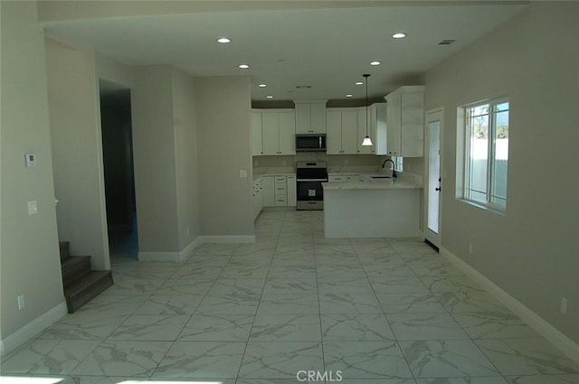 kitchen featuring pendant lighting, kitchen peninsula, sink, appliances with stainless steel finishes, and white cabinets