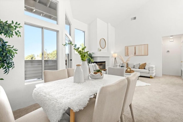 dining space with high vaulted ceiling, a tile fireplace, and light carpet