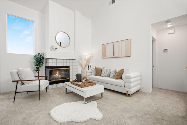 carpeted living room featuring a tiled fireplace and high vaulted ceiling