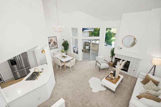 living room with light colored carpet, a notable chandelier, a tile fireplace, sink, and high vaulted ceiling