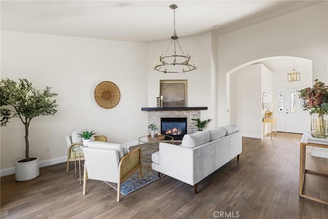 living room with dark hardwood / wood-style flooring, a chandelier, and a stone fireplace