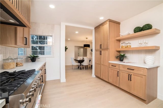 kitchen featuring pendant lighting, light brown cabinets, decorative backsplash, stainless steel stove, and light hardwood / wood-style flooring